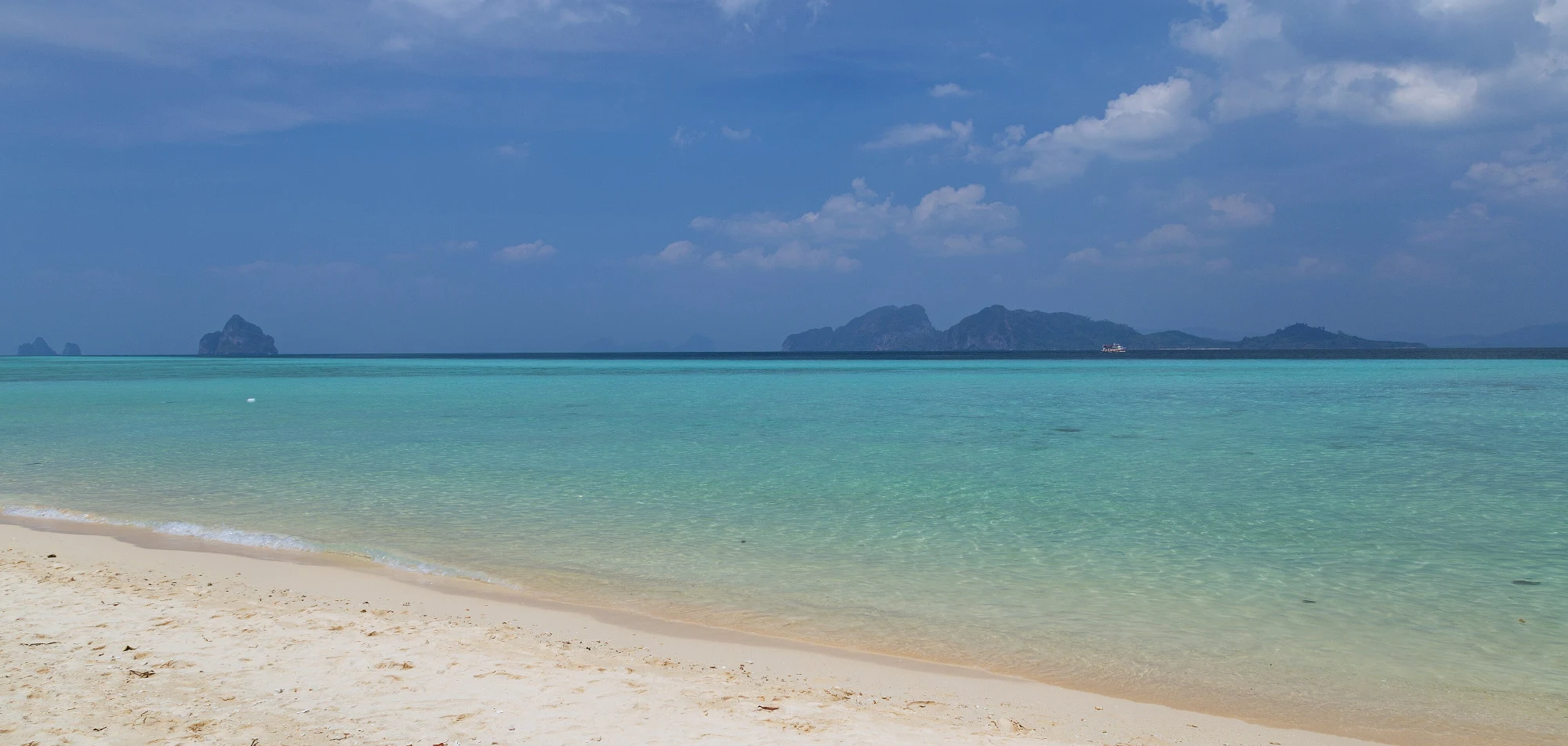 Shallow turquoise water over sand and seagrass off Ko Kradan in Trang, with limestone islands on the horizon