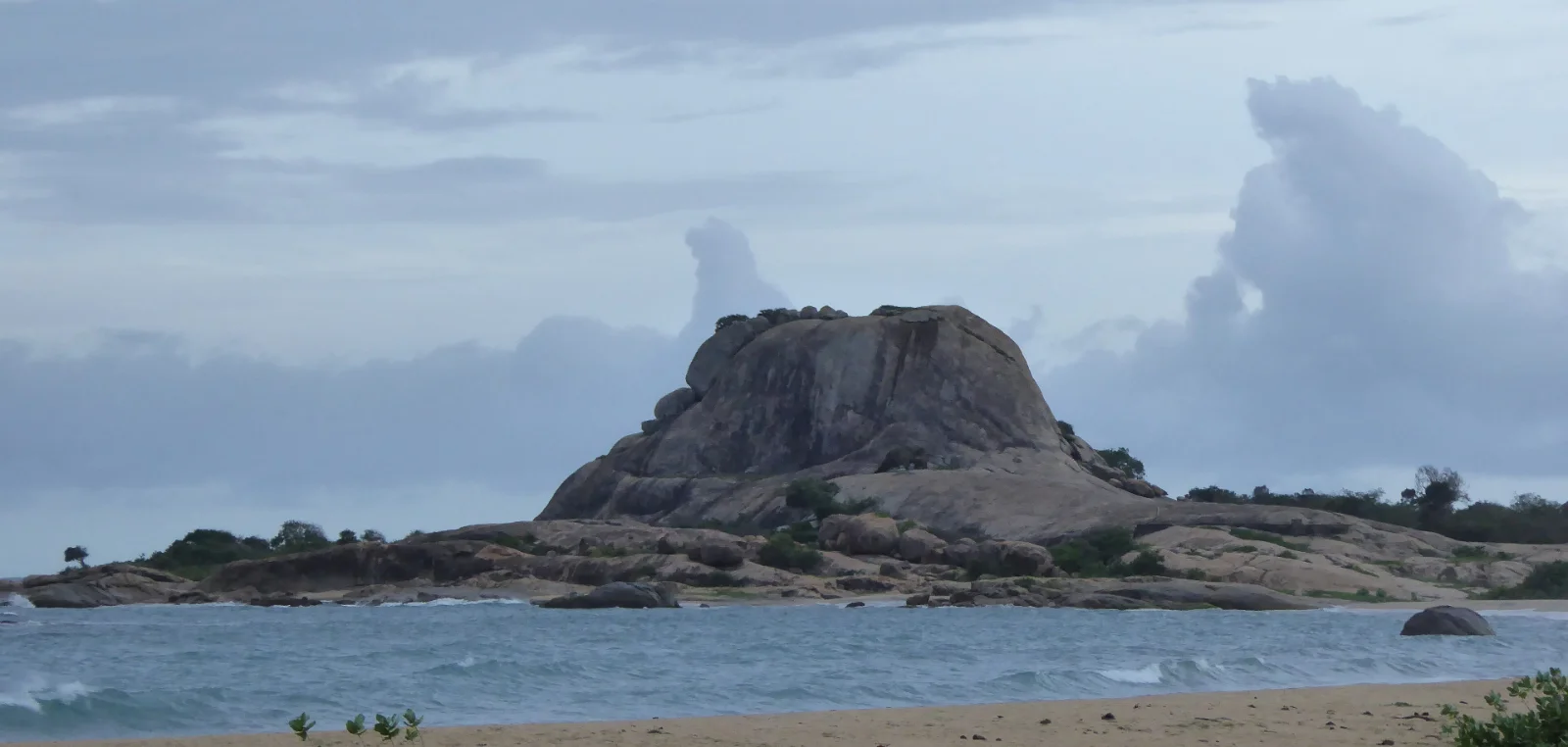 A granite outcrop rising from coastal scrub under a wide sky.